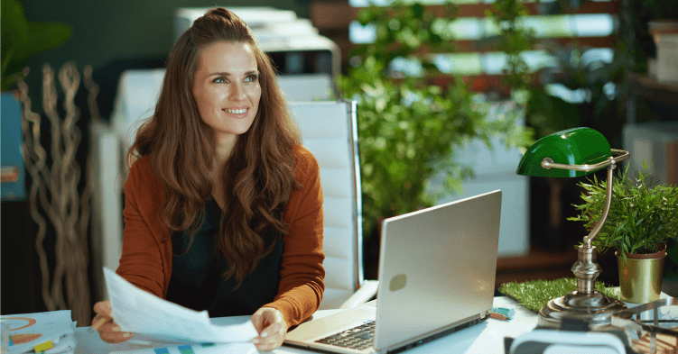 Business woman holding papers while seated at a laptop