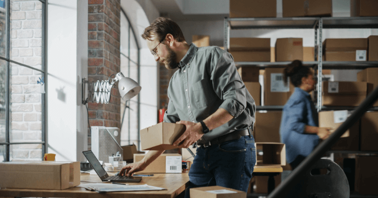 Small business owner typing on laptop while standing up and holding a small box