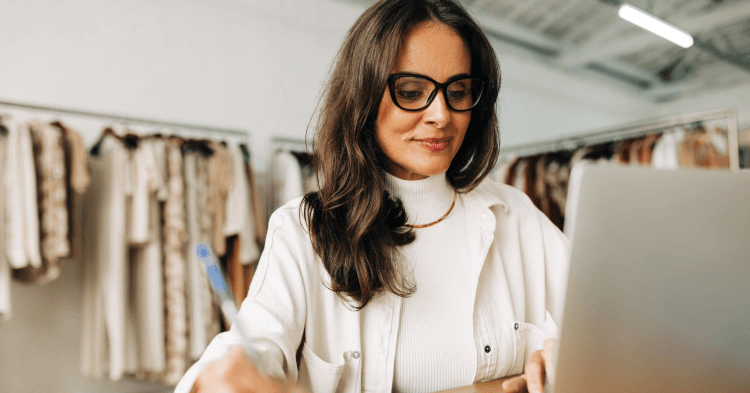 Female small business owner wearing glasses smiles at her laptop.