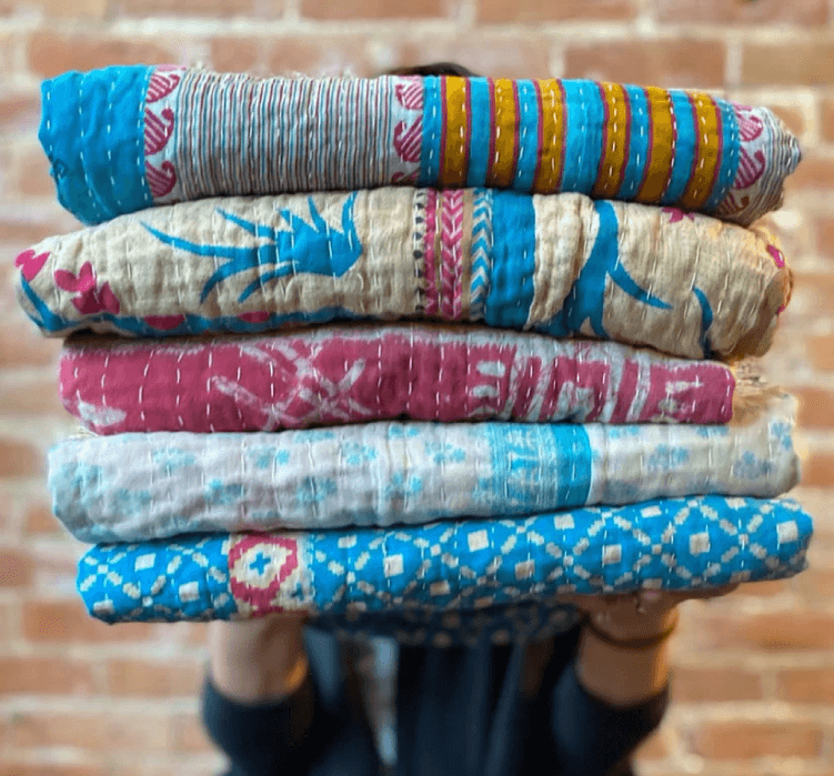Person holding a stack of brightly-colored blankets.
