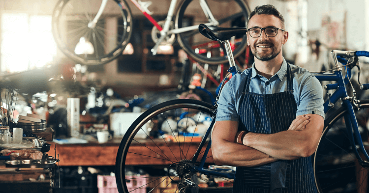 Small business owner in an apron standing in front of his bike workshop
