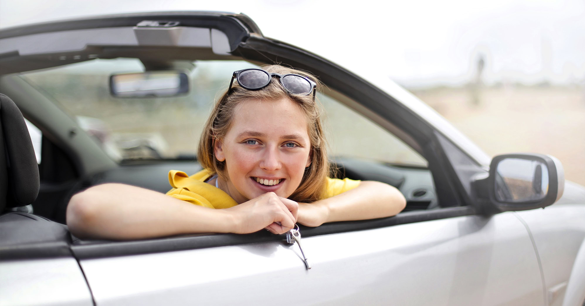 A photo with a woman in a car holding a key.